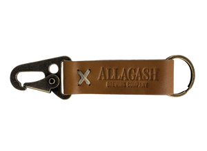 A brown leather keychain with a metal ring and snap hook, featuring an embossed logo that reads 'Allagash Brewing Company'.