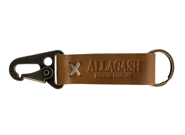 A brown leather keychain with a metal ring and snap hook, featuring an embossed logo that reads 'Allagash Brewing Company'.