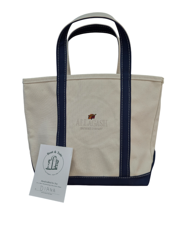 Beige tote bag with navy handles and a tag on a white background